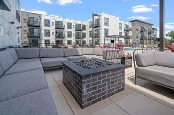 furnished patio with couches and a fire pit with an apartment building in the background
